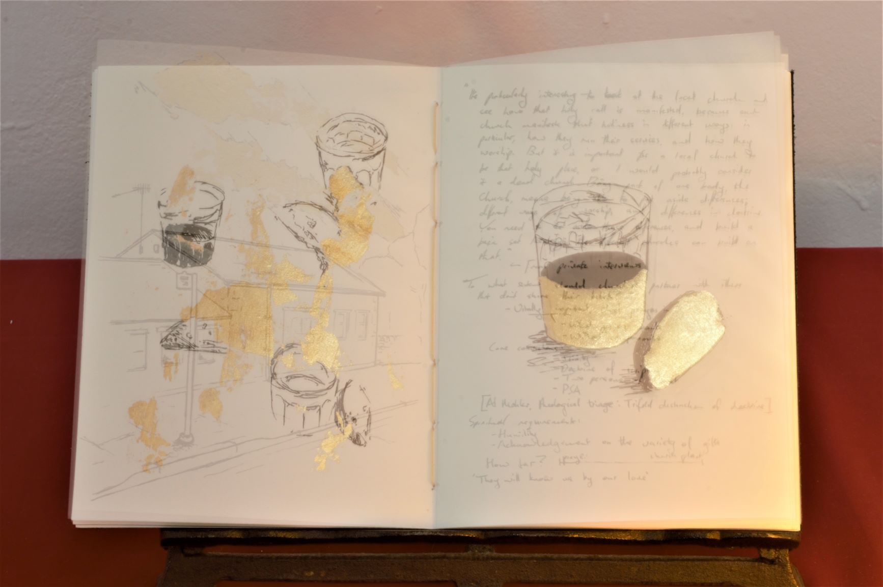 A duel exposure image of a handmade book, one leaf showing a drawing of a church and some notes, the other showing some sketches of communion bread and win with gold leaf